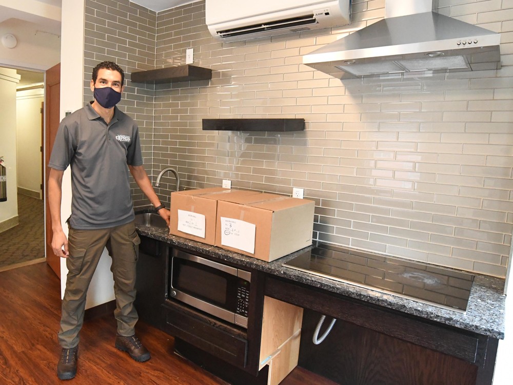 A Campus Services Express team member stands in a residence hall kitchen with two packages.