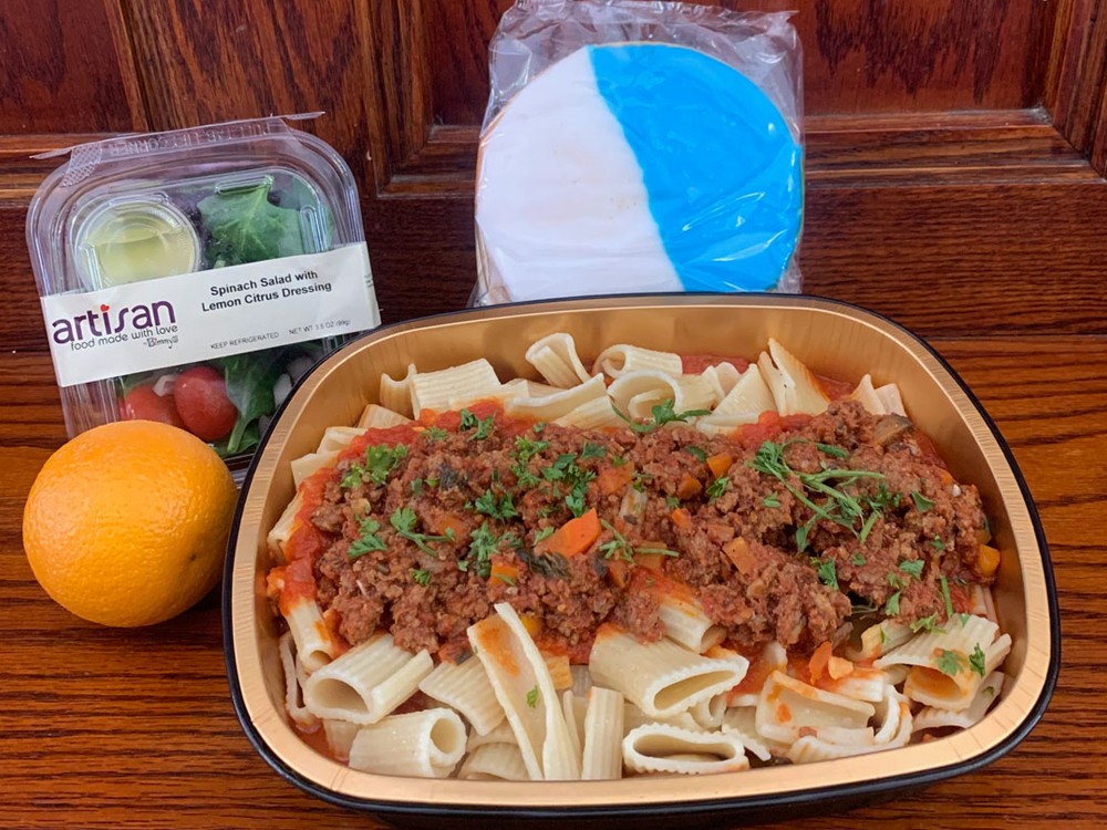 A pasta and meat sauce meal prepared for students during the delivery period, with a salad, orange, and large white and blue cookie.