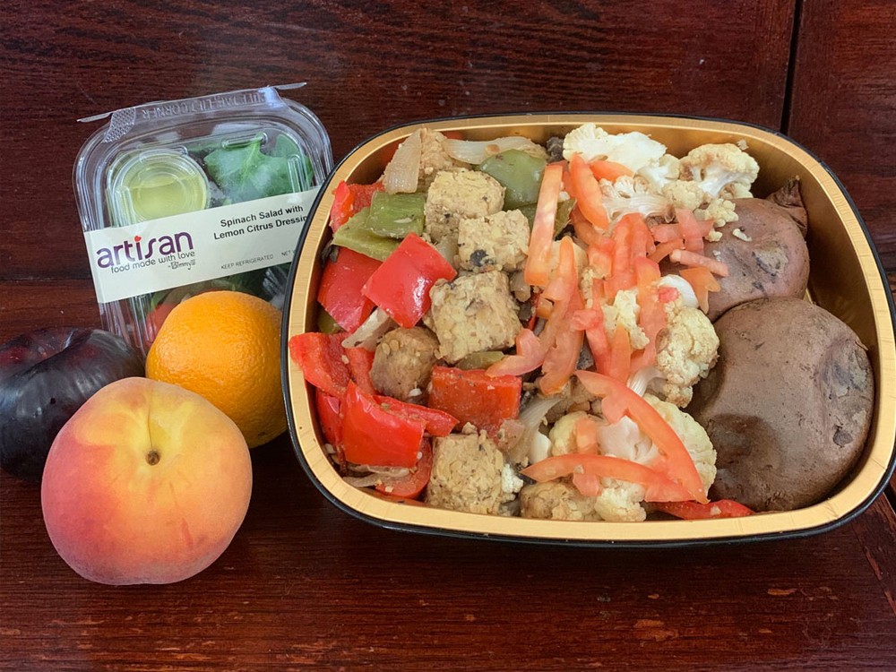 A vegetarian/vegan meal prepared for students during the delivery period including a salad, a plum, peach, and orange.