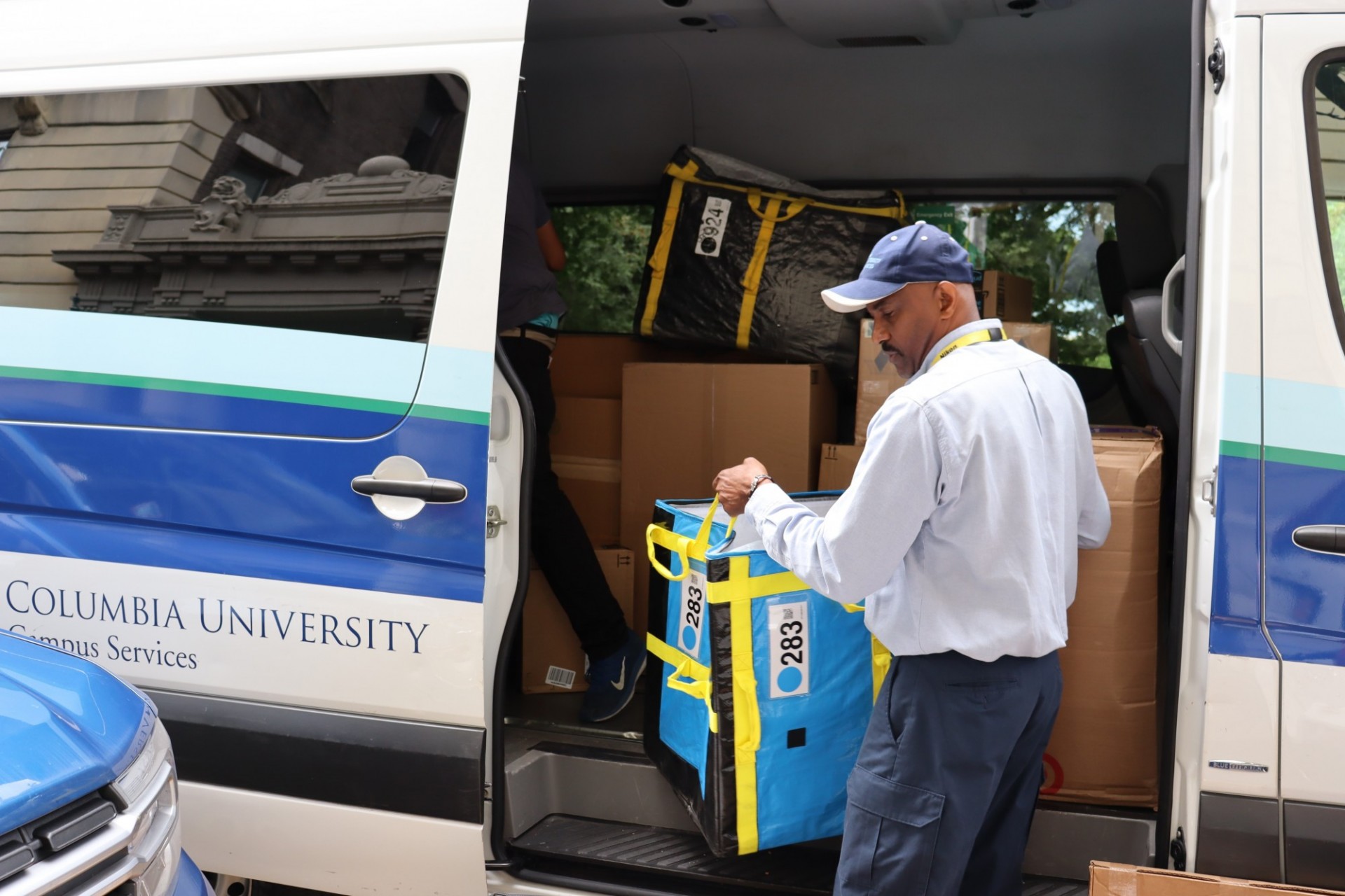 Mail team member unloading tote bags of packages from Campus Services bus