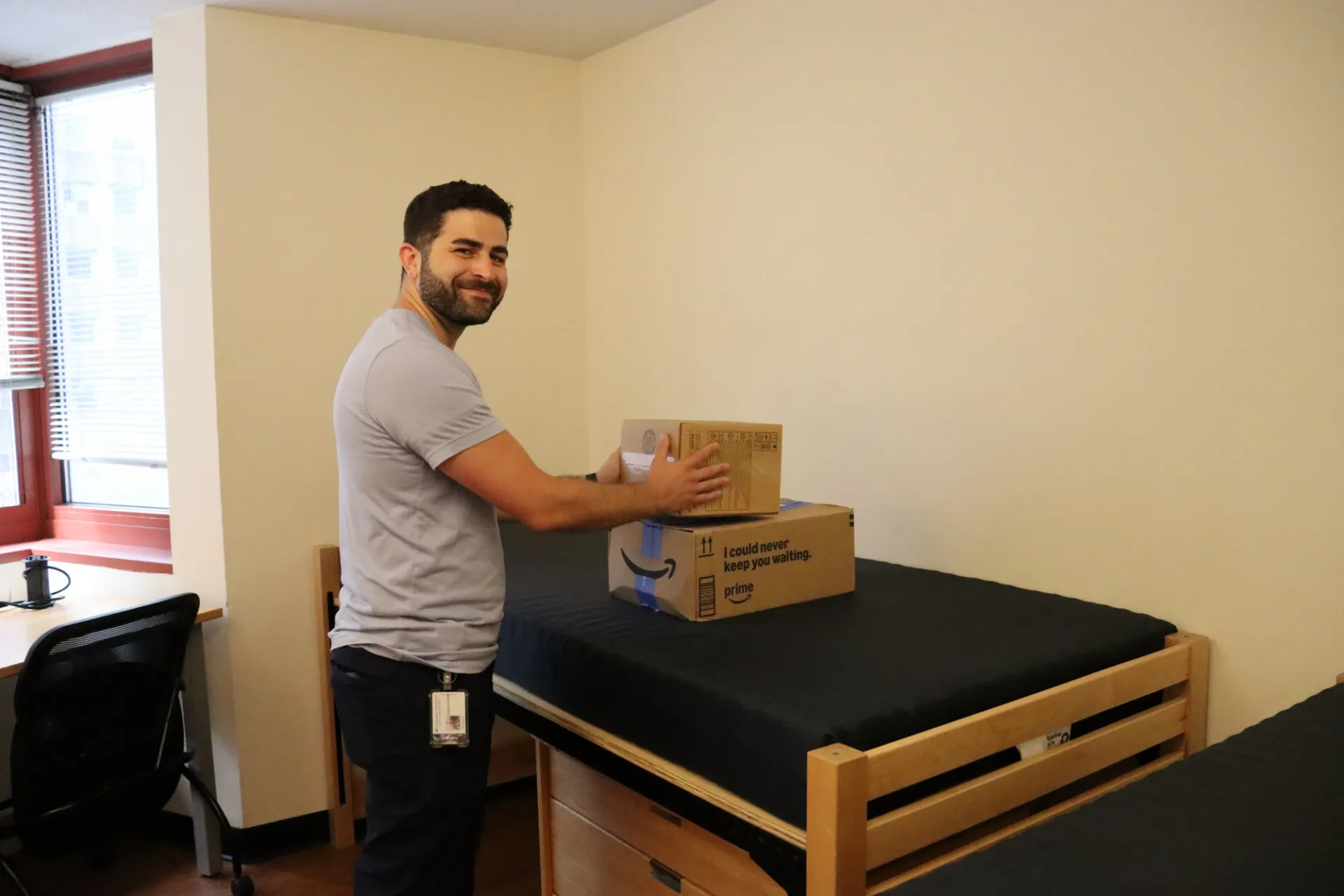 Campus Services staff member places delivery boxes on a bed inside a residence hall room during student move-in preparations.
