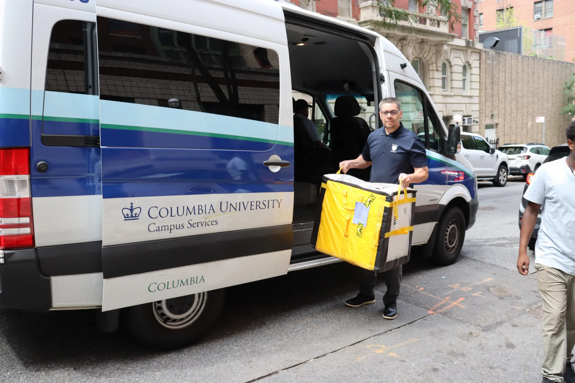 Campus Services staff member unloads a package bin from a Columbia University Campus Services vehicle as part of residence hall package delivery and move-in support.