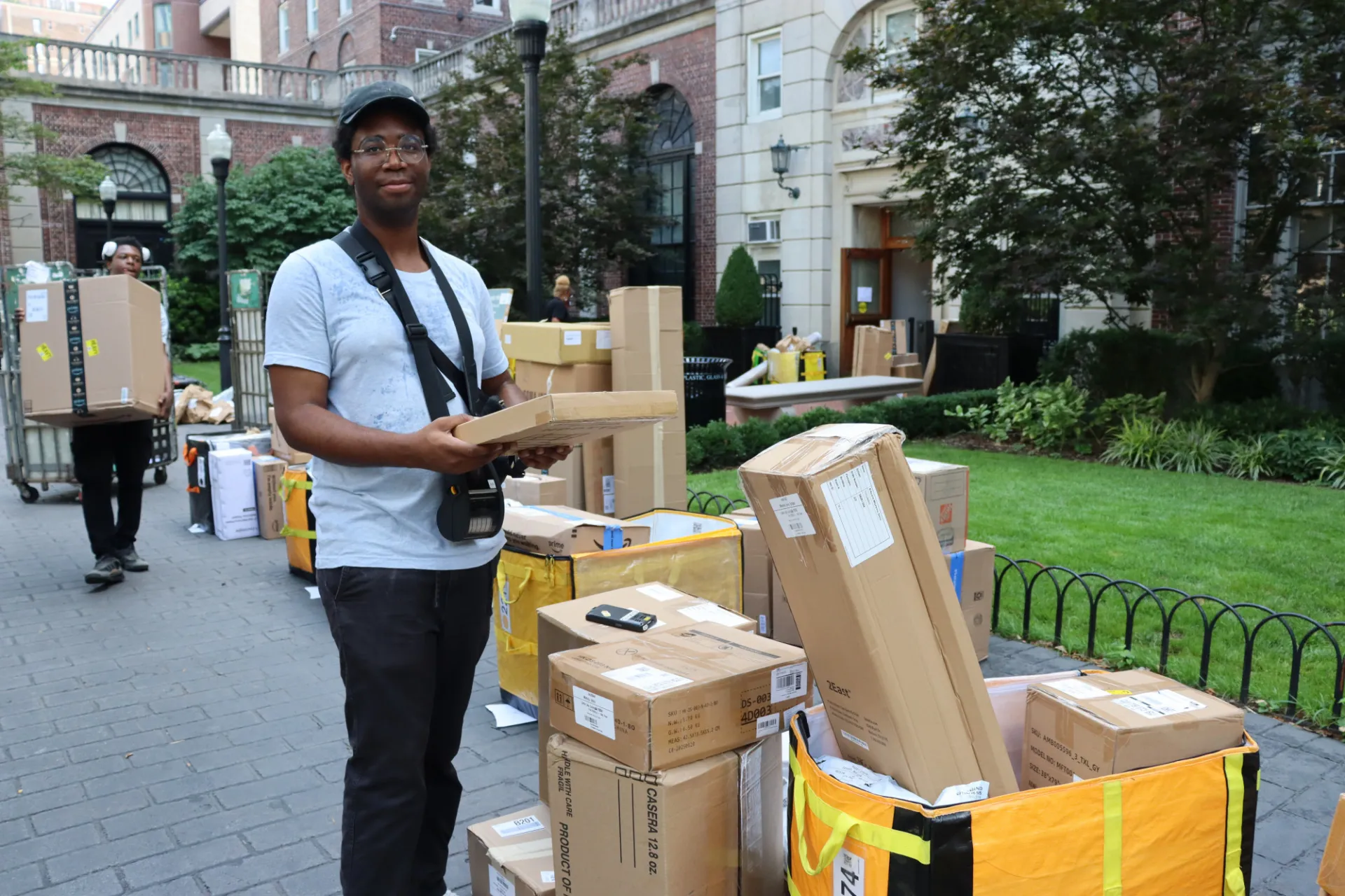 Campus Services employee sorts and handles incoming packages beside delivery bins and stacked boxes outside a residence hall during student move-in operations.